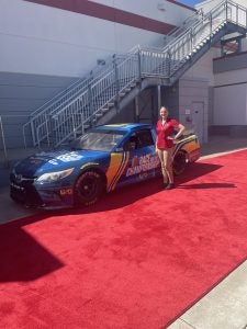 School of Hospitality Leadership student Makayla Lane stands next to NASCAR car