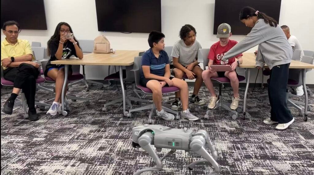 Students interact with a robotic dog during ECU’s AI Robotics Workshop at the Isley Innovation Lab, while others observe and take photos in a classroom setting.