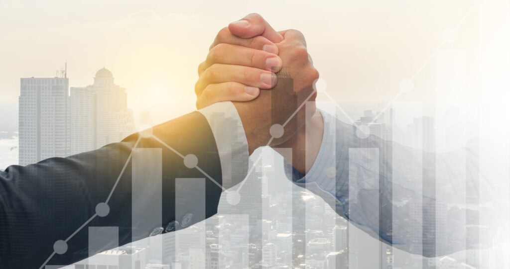 Two hands clasped in a firm handshake, symbolizing partnership and collaboration, overlaid with a city skyline and upward-trending bar and line graphs representing business growth and success.