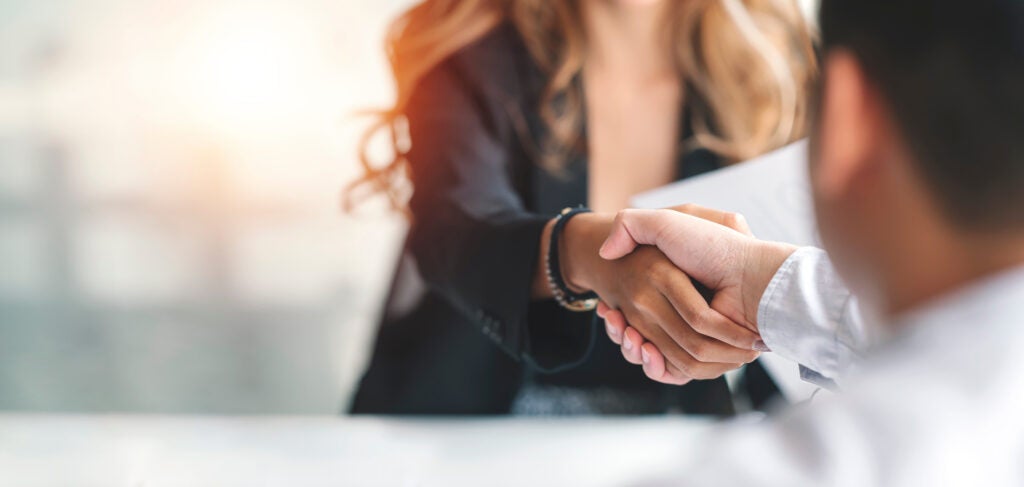 Close-up of a handshake between a woman in business attire and another person, symbolizing agreement or partnership in a professional setting.