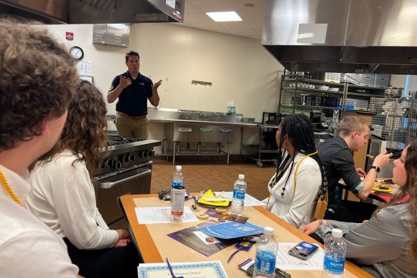 Waffle House rep Benjamin Pratt speaks to SHL students in an industrial kitchen setting. 