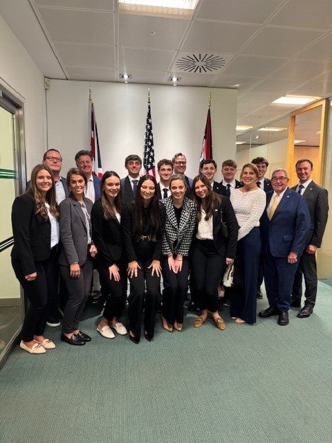 A group of ECU business students and faculty pose with staff in front of U.S. and U.K. flags at Cincinnati Global's office in London.