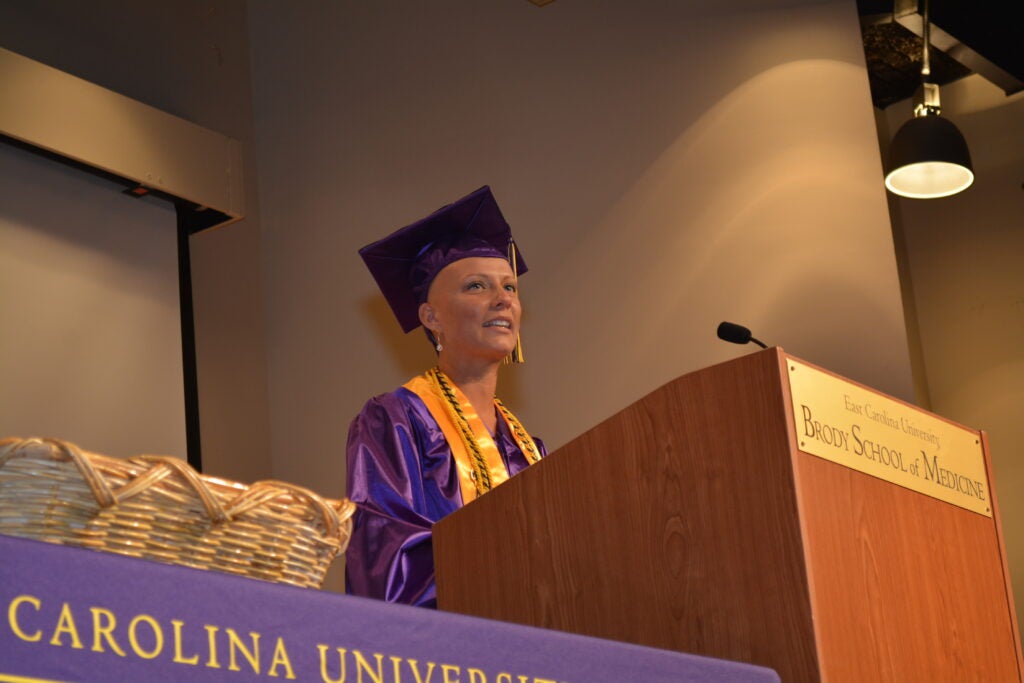 Emily Osborne stands at podium in graduation gown and speaks to gradudation audience. 