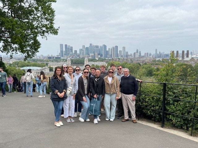 Students and faculty pose at a scenic overlook in Greenwich Park with the London skyline and historic Royal Naval College in the background.