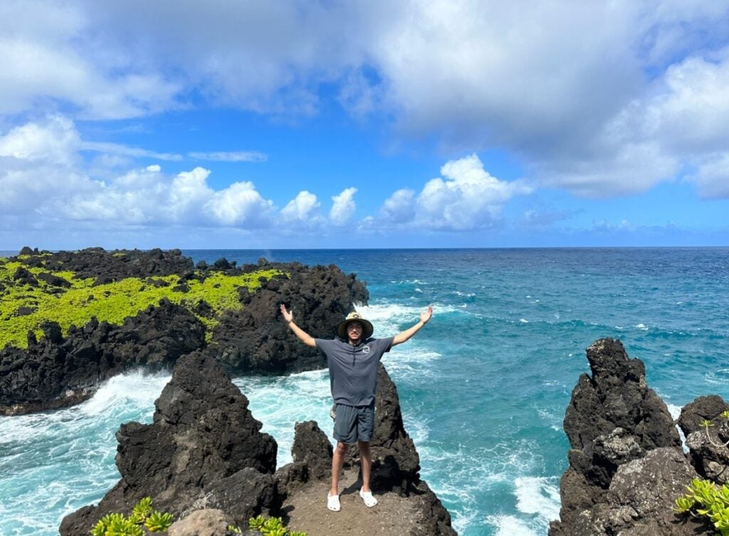 Justin Aldrich, arms out wide, stands on a rocky beach.