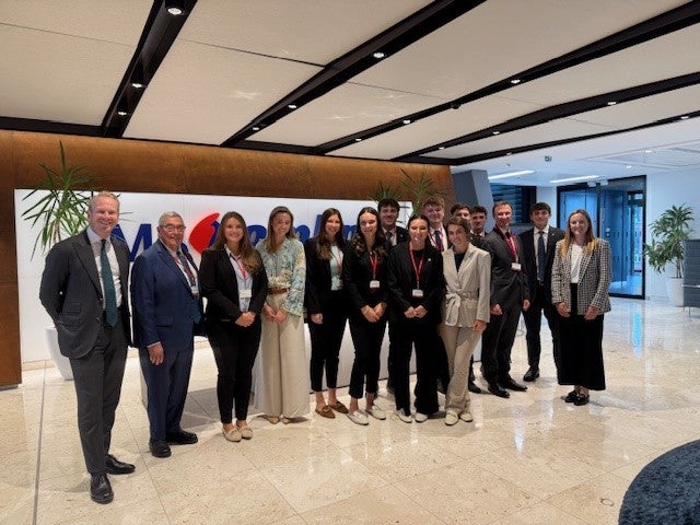 College of Business students dressed in business attire pose with faculty and hosts in the corporate lobby of MS Amlin, a reinsurance company in London.