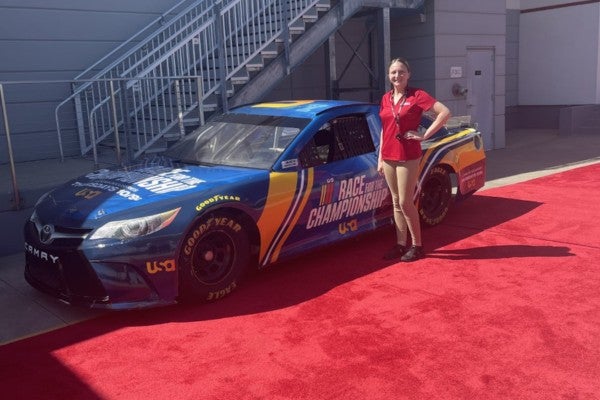 Intern stands in front of NASCAR car. 