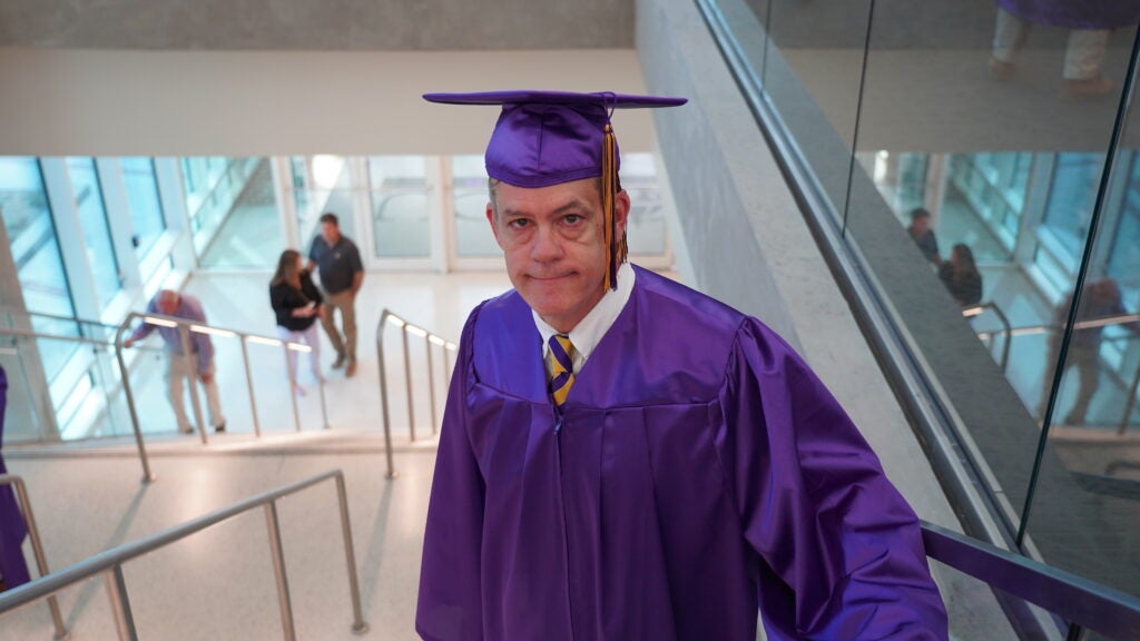 Toby Barbour, dressed in graduation cap and gown, climbs stairs in ECU student center.