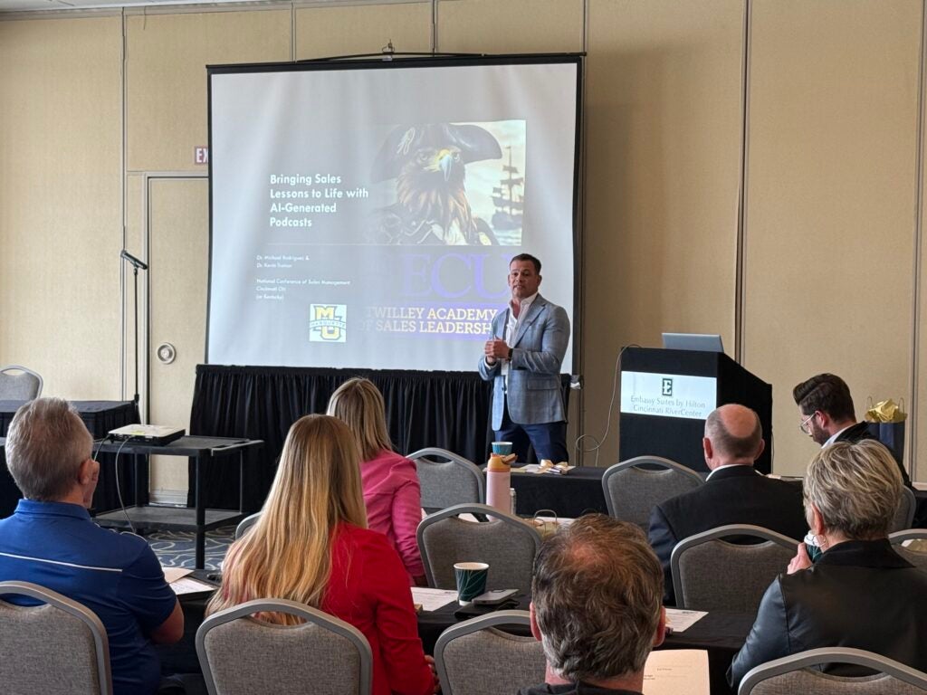 Dr. Michael Rodriguez presents on AI-generated podcasts at the NCSM conference in Cincinnati, with attendees seated in front of him.