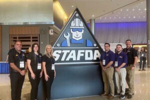 College of Business faculty and students flank STAFDA logo in a conference lobby.